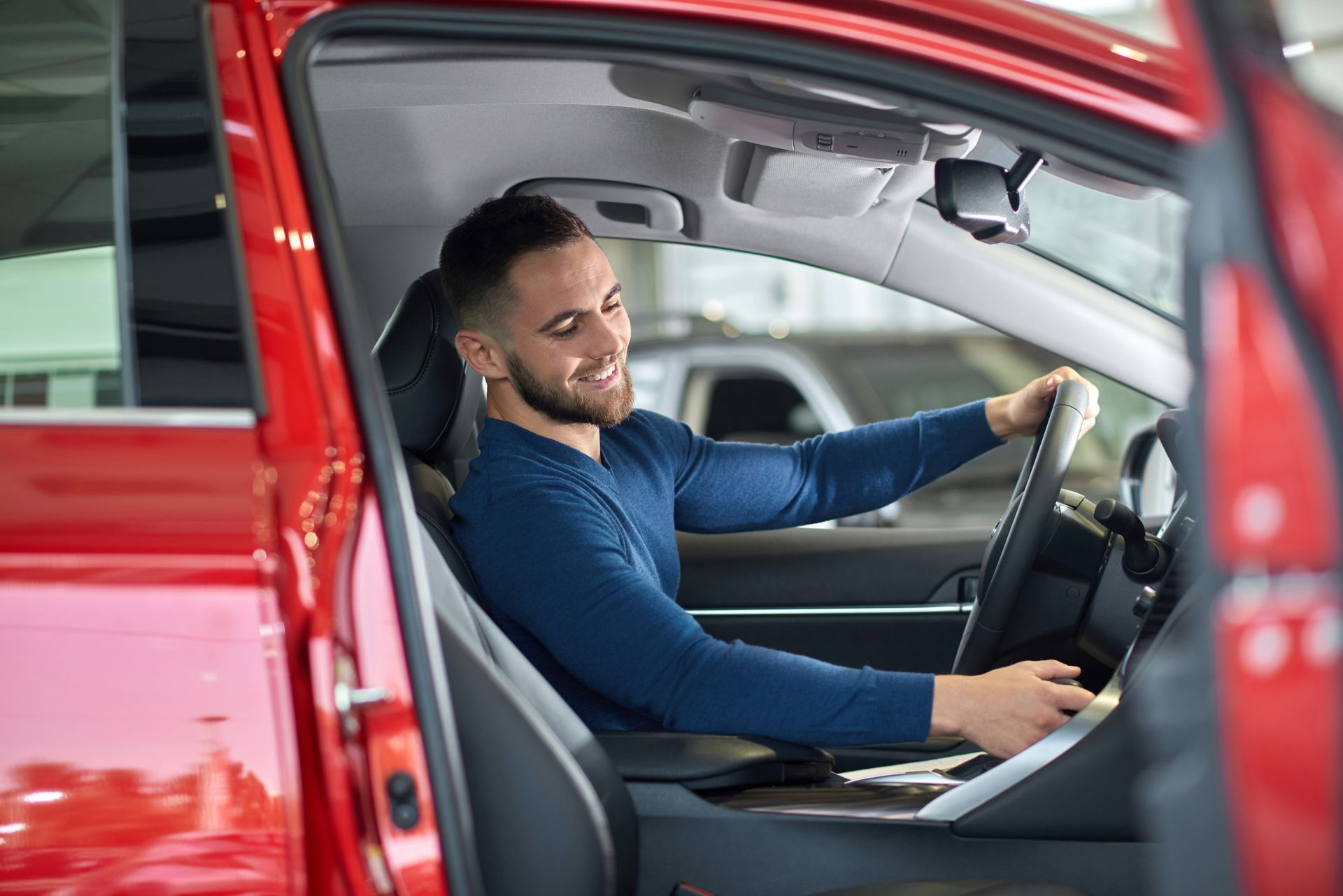 A man is sitting in the driver 's seat of a red car. 