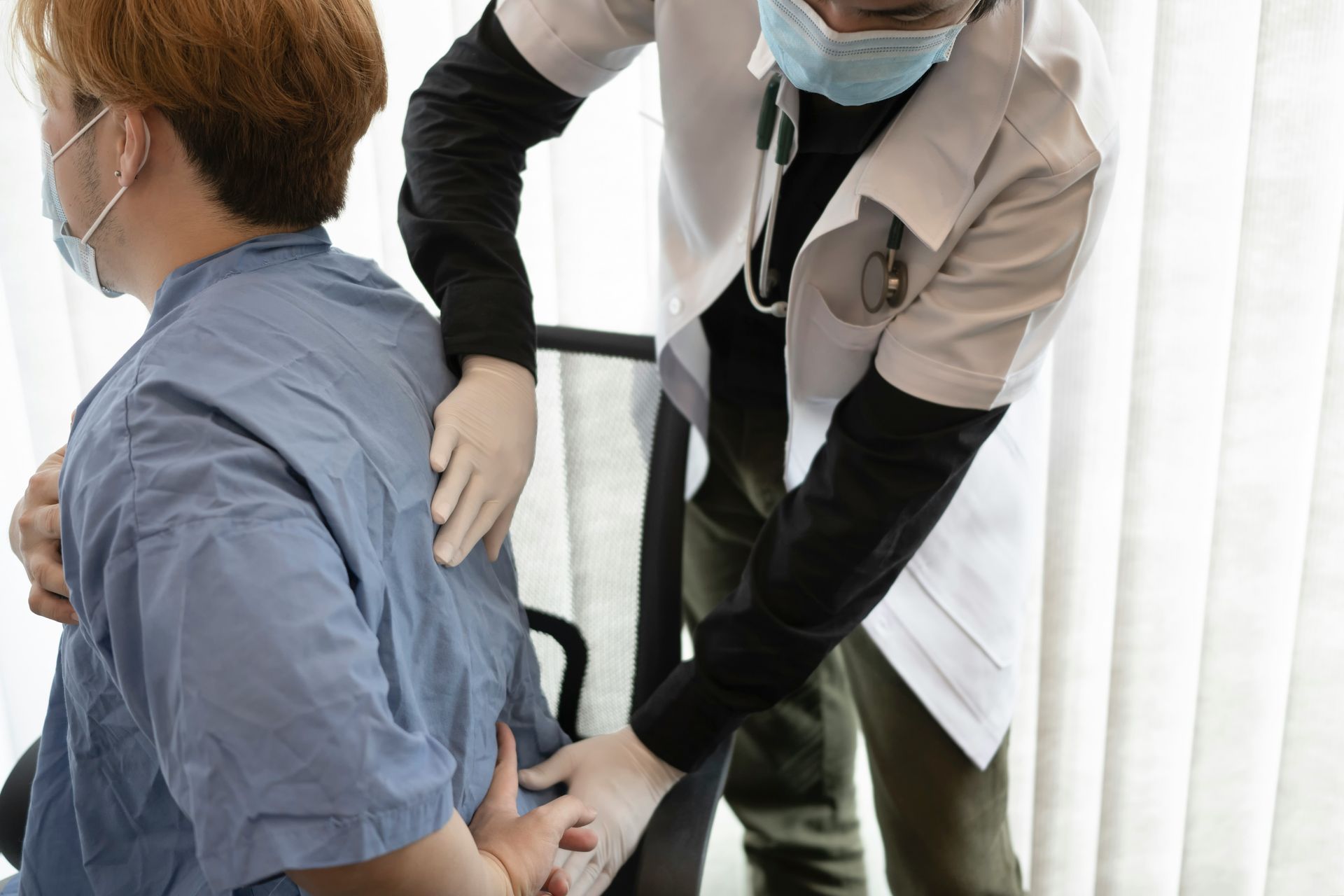 A doctor is examining a patient 's back while wearing a mask. 