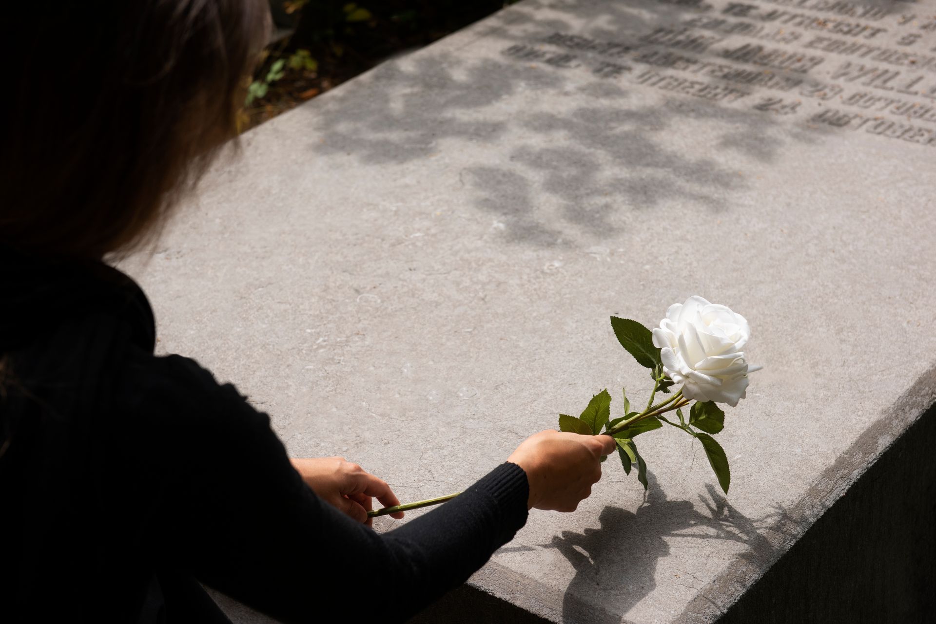 A woman is holding a white rose in front of a grave. 