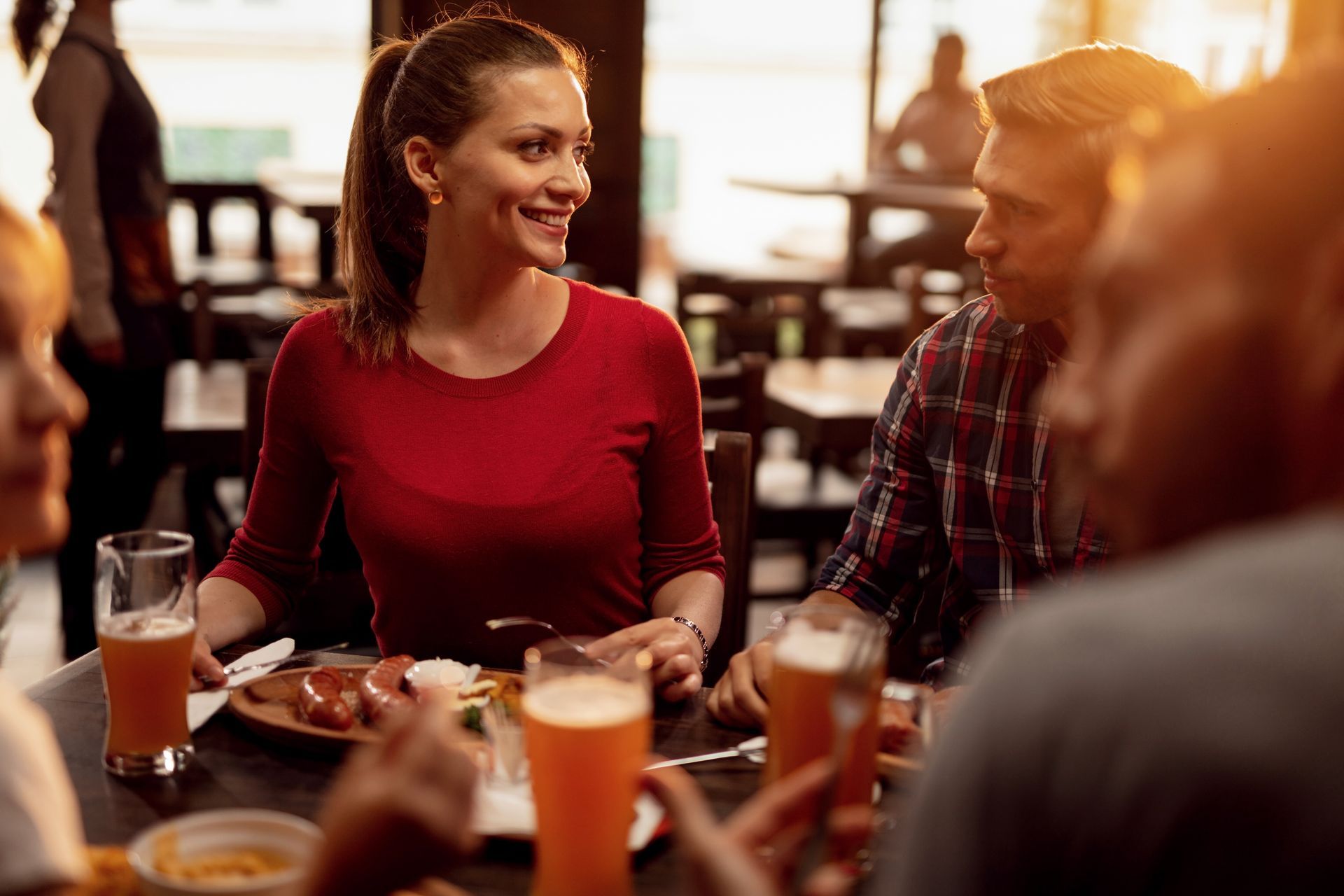 A group of people are sitting at a table in a restaurant eating food and drinking beer. 