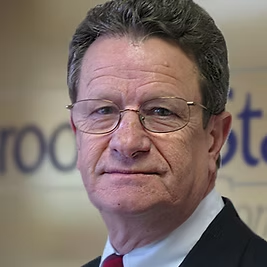 A man wearing glasses and a suit and tie is looking at the camera.