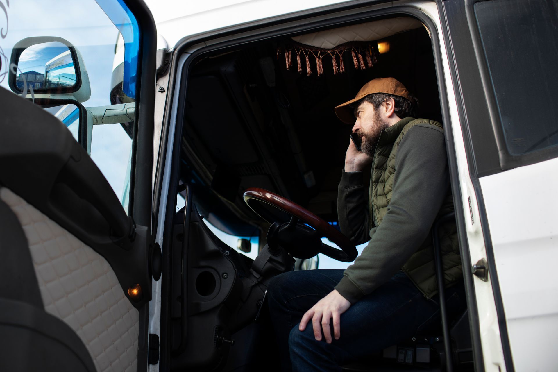 A man is sitting in the driver 's seat of a truck talking on a cell phone. 