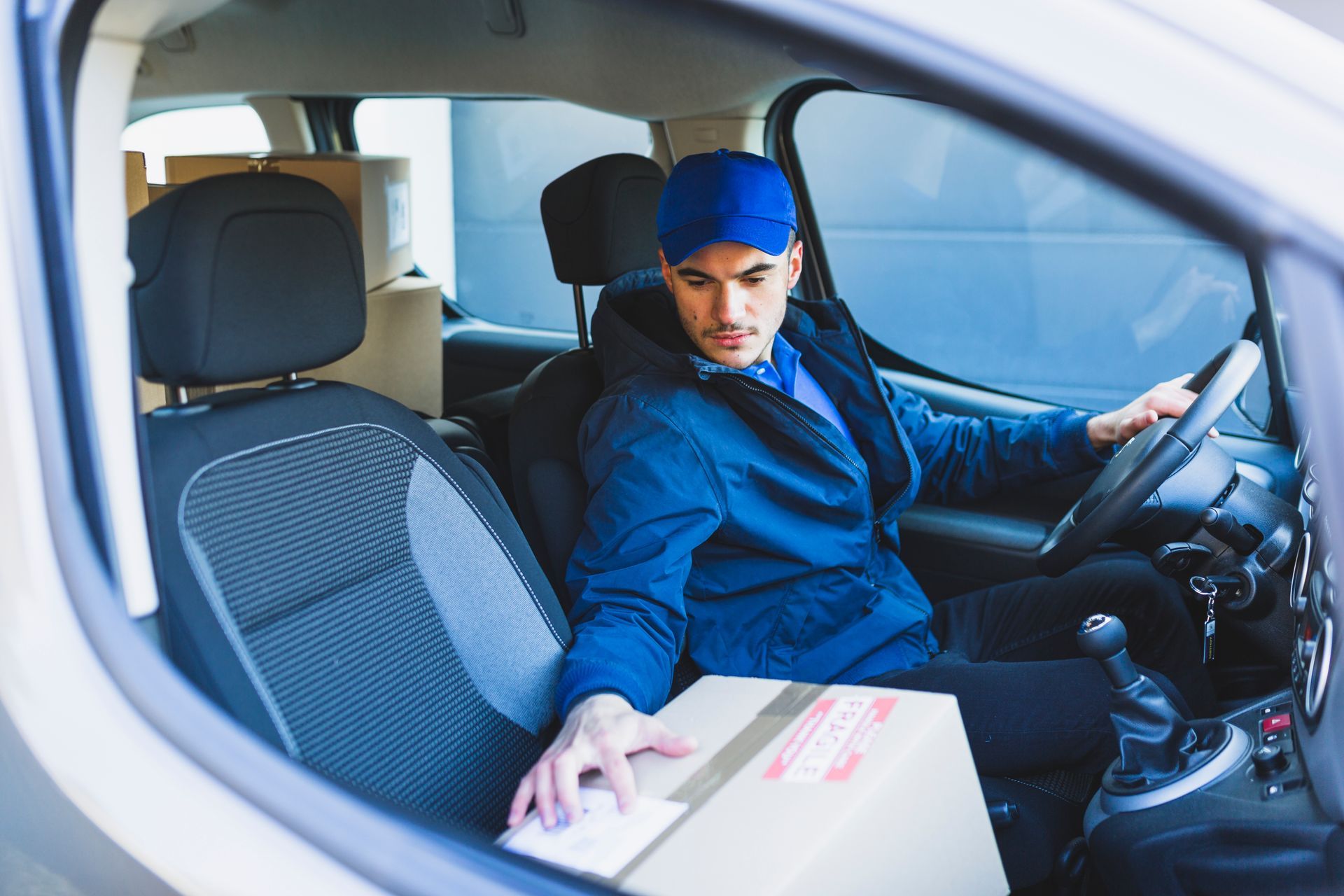 A delivery man is sitting in the driver 's seat of a van holding a cardboard box.
