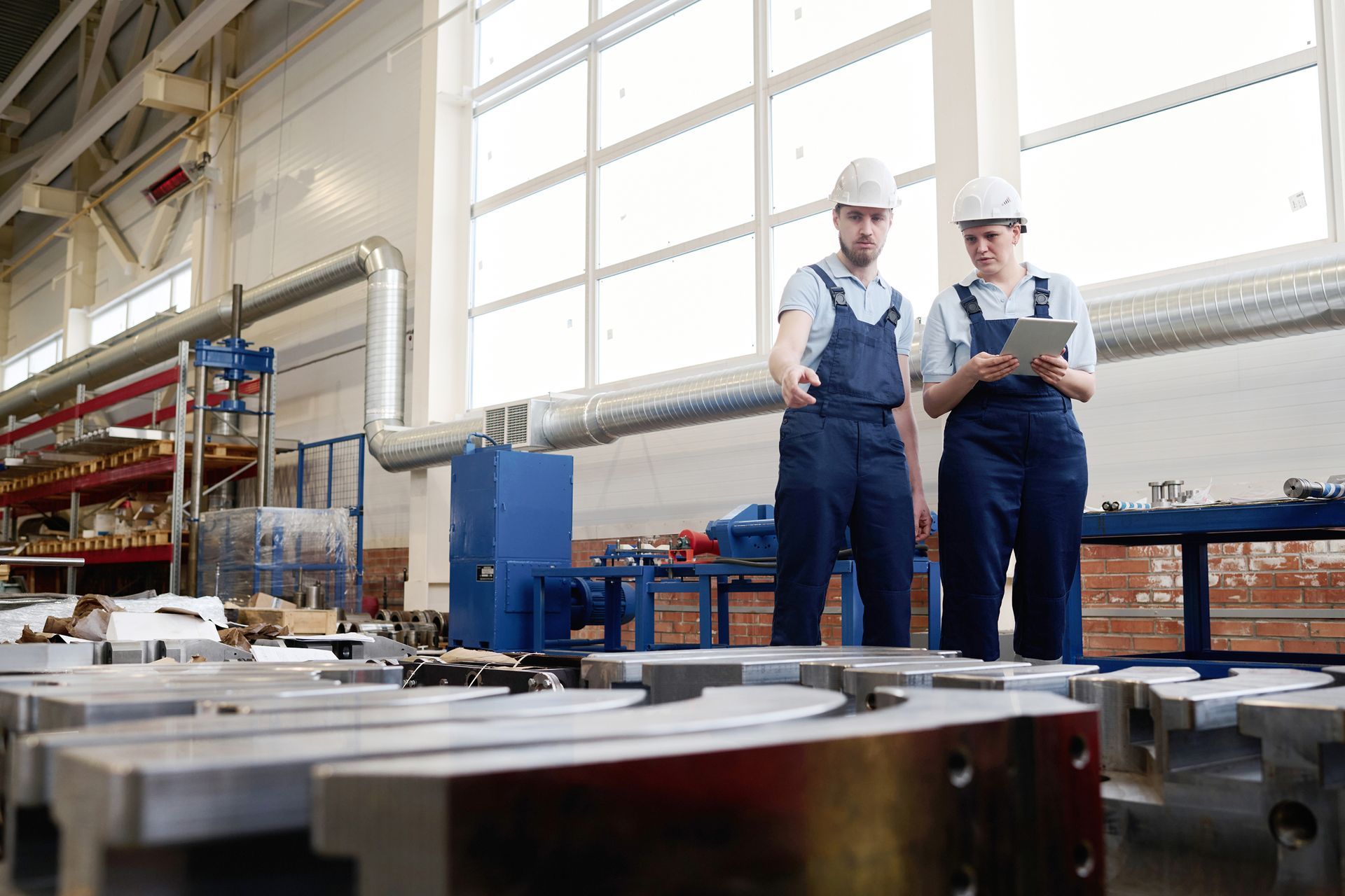 A man and a woman are standing in a factory looking at a tablet. 