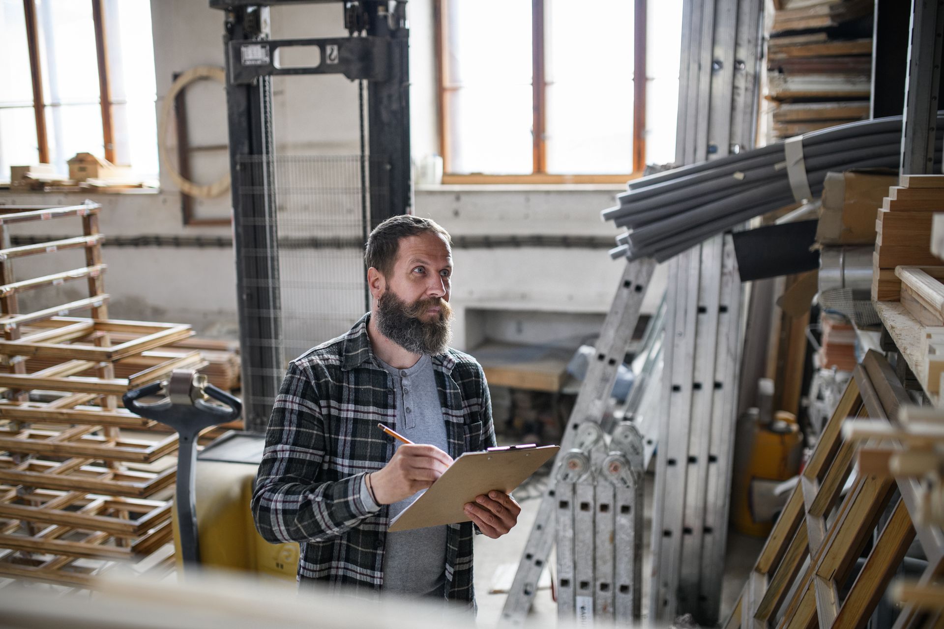 A man is standing in a warehouse looking at a clipboard.
