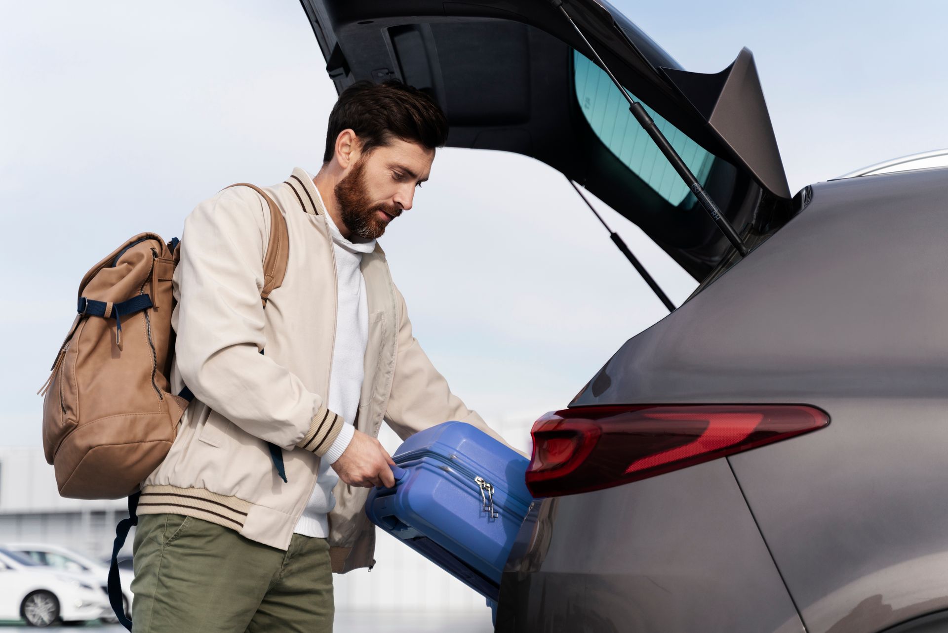 A man is putting a suitcase in the back of a car. 