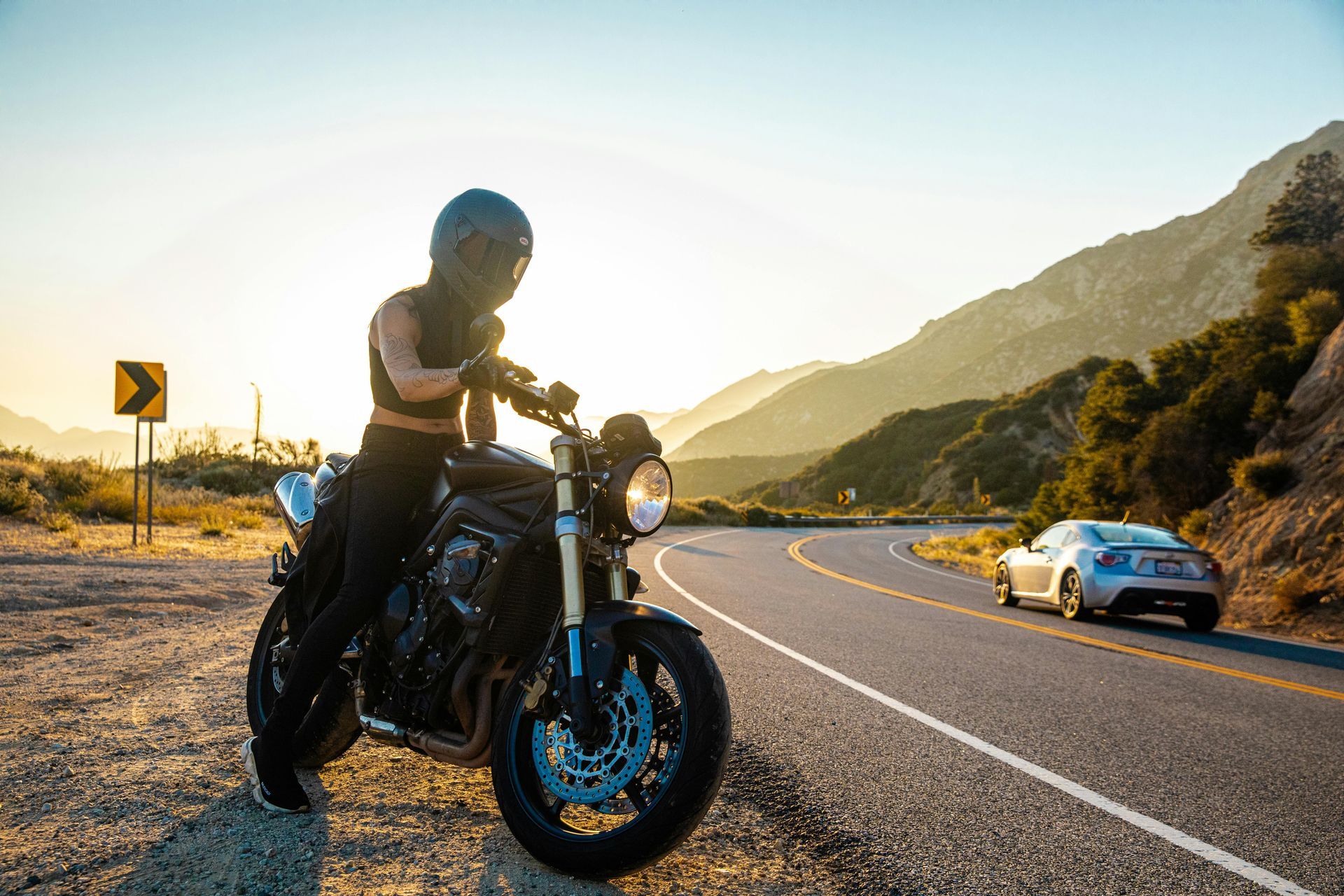 A woman is sitting on a motorcycle on the side of a road. 