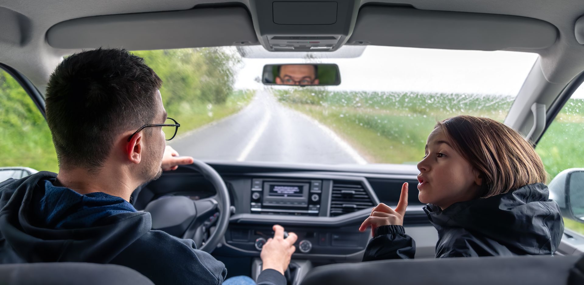 A man and a woman are sitting in a car talking to each other. 