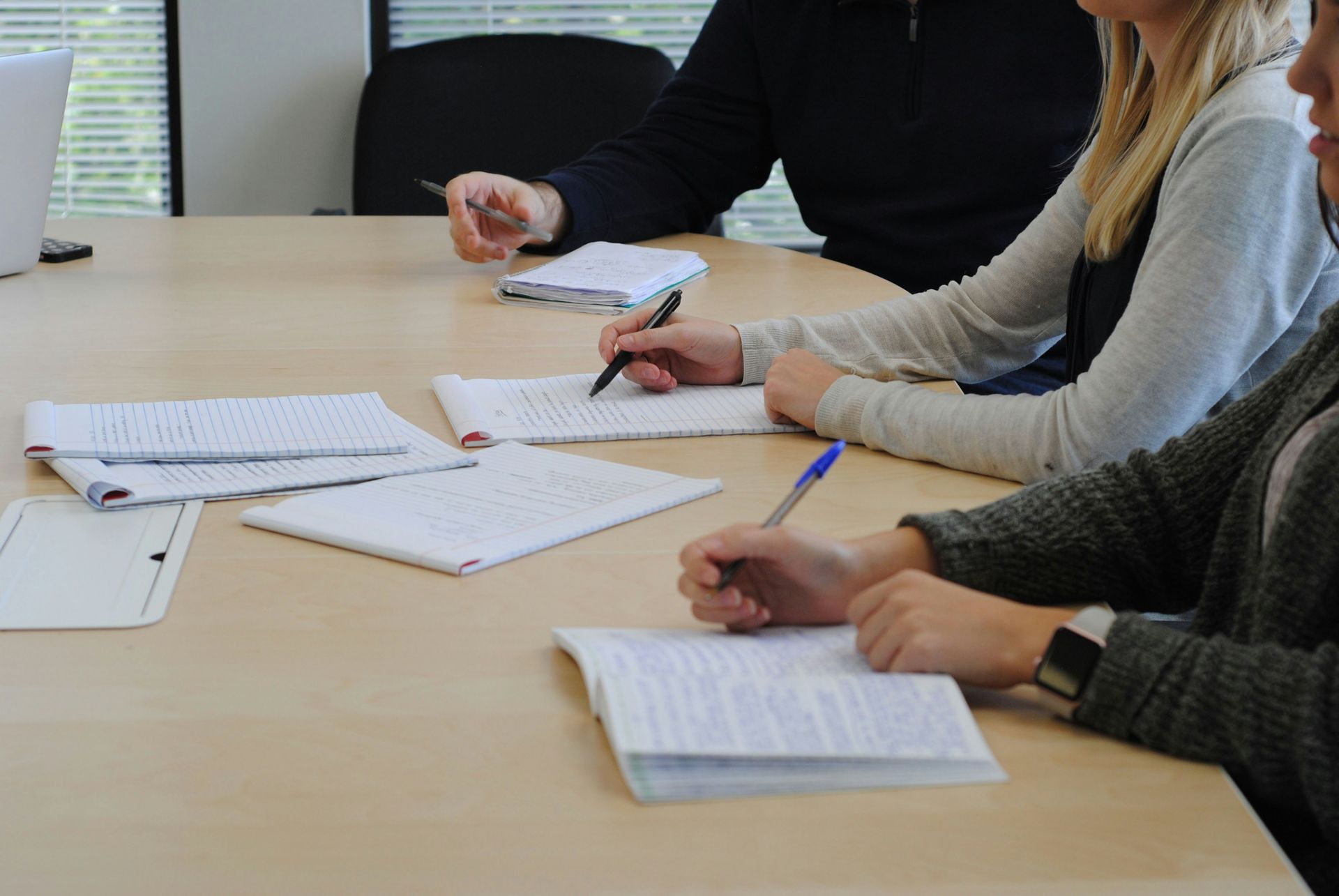 A group of people are sitting at a table writing in notebooks. 