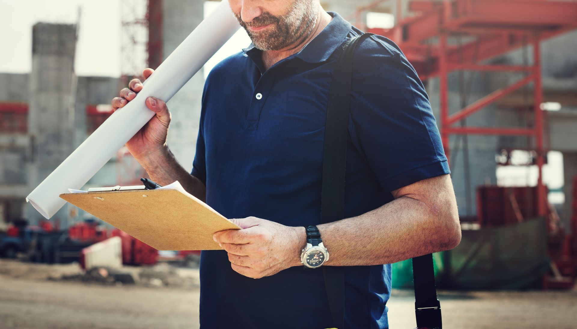 A man is holding a blueprint and looking at a clipboard. 