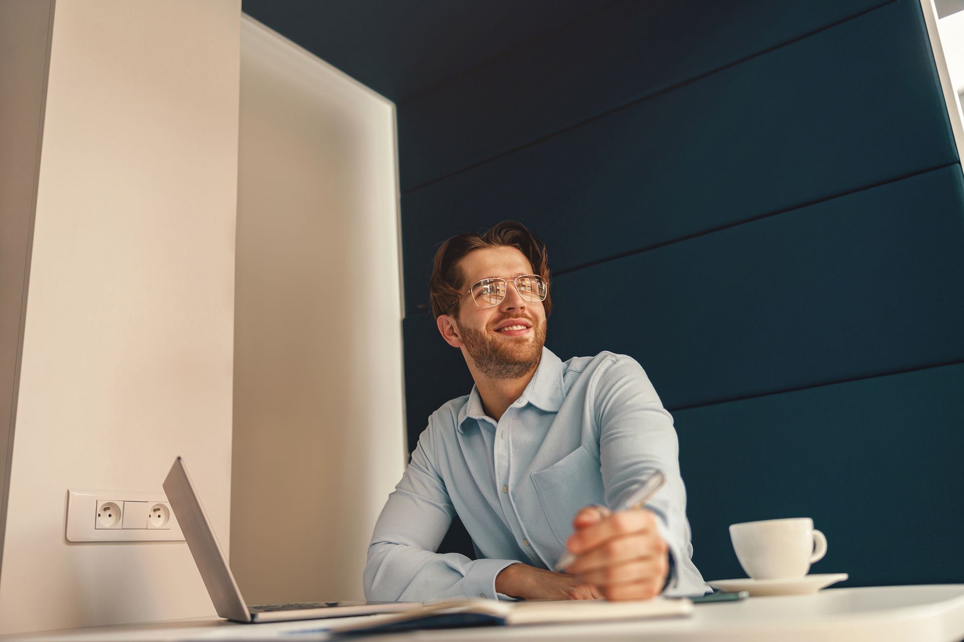 A man is sitting at a table with a laptop and a cup of coffee. 