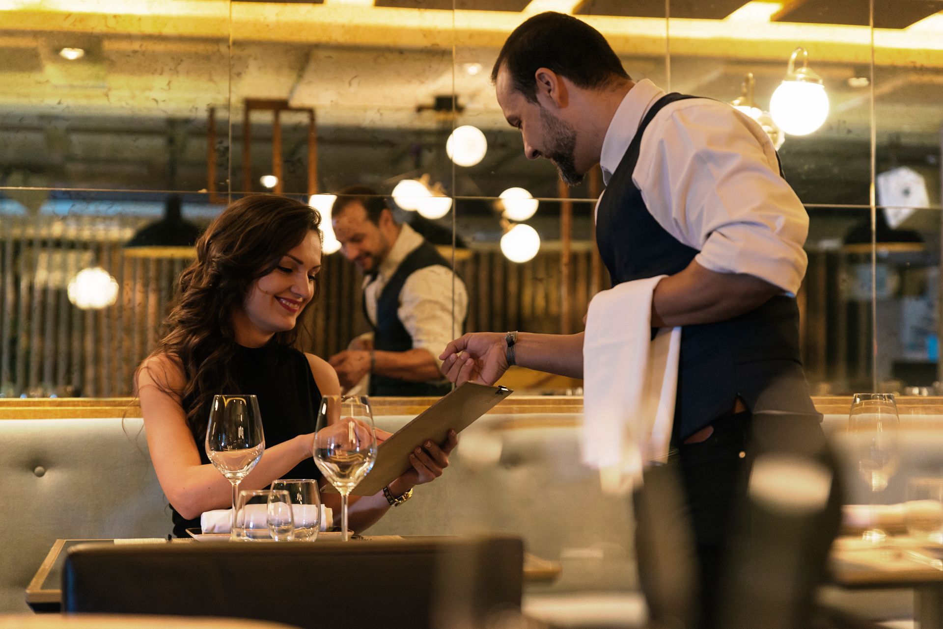 A man is serving a woman in a restaurant while she looks at a menu. 