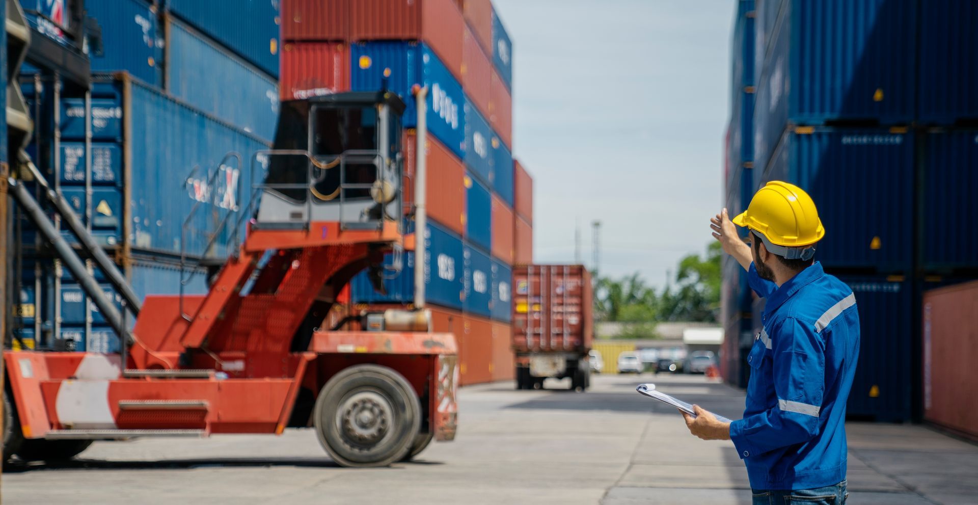 A man in a hard hat is standing in front of a forklift in a warehouse. 