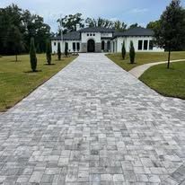 A large white house with a driveway leading to it is lit up at night.