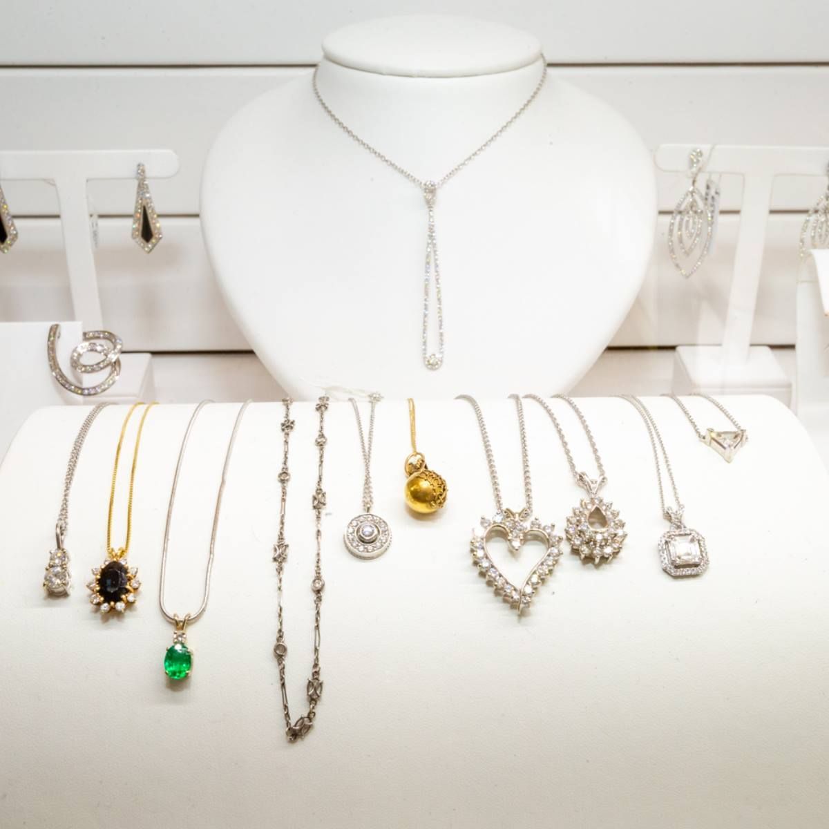 Assorted necklaces and earrings displayed on white jewelry stands and busts