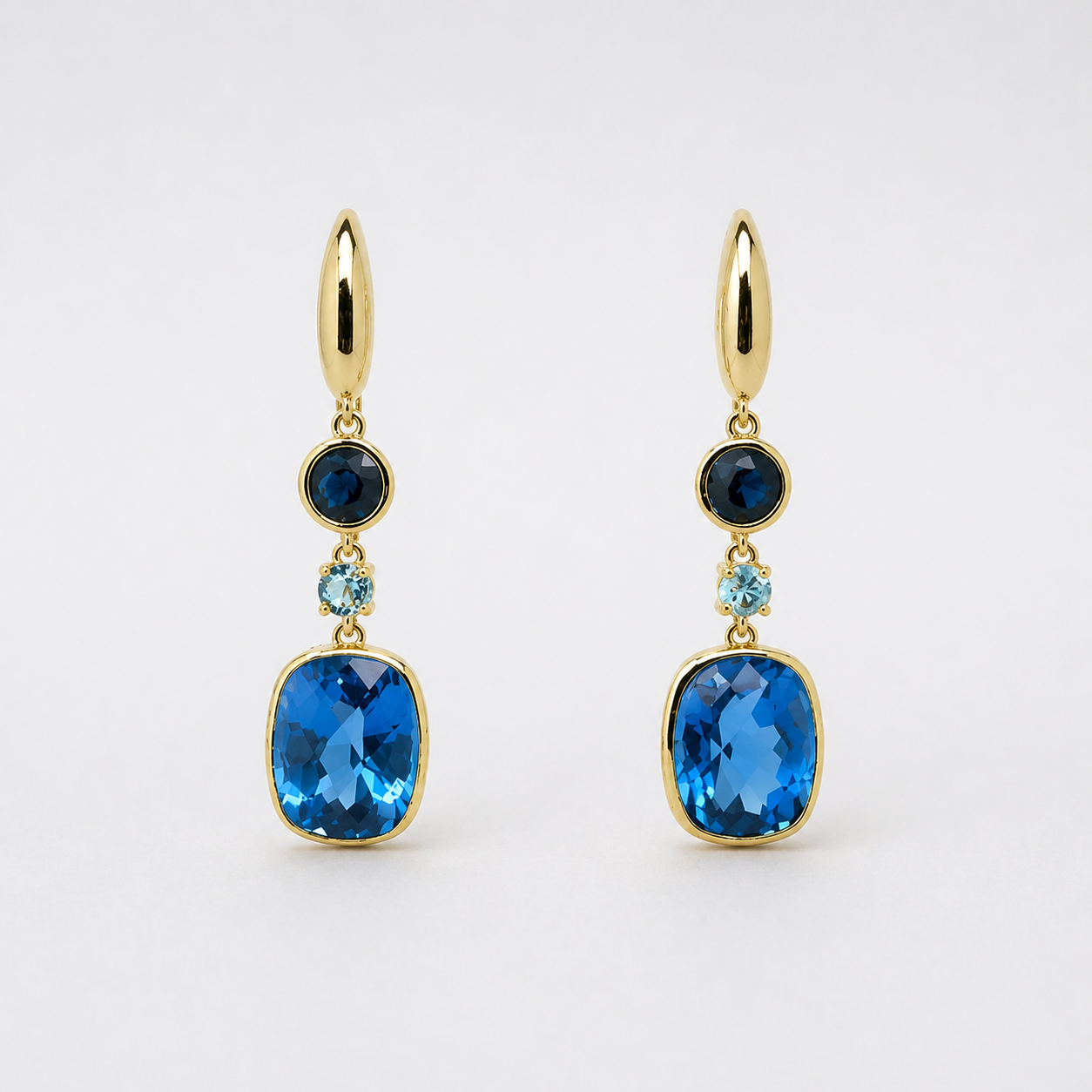 Pair of gold dangling earrings with blue gemstones, featuring oval and rectangular stones.