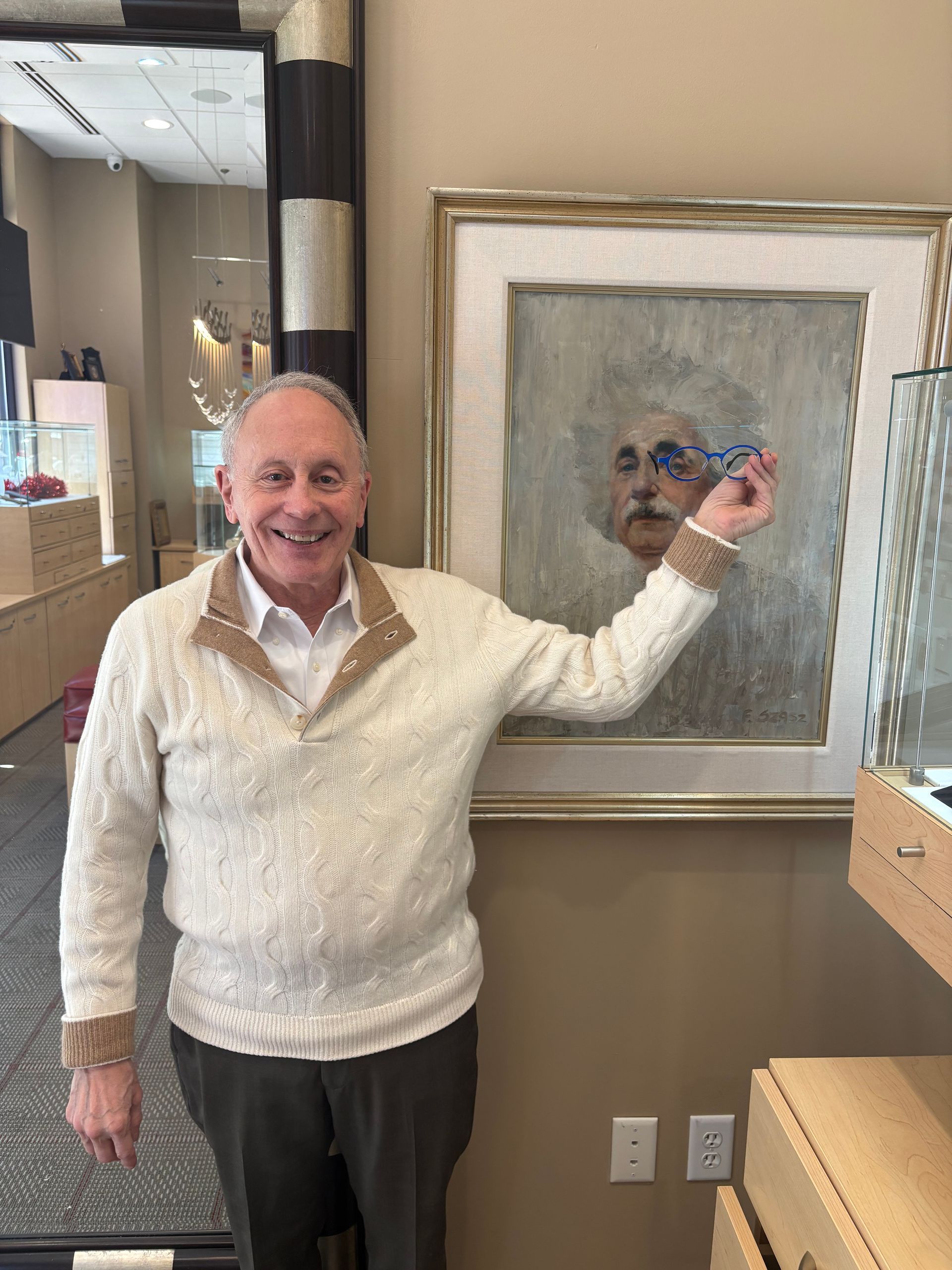 Man smiling in a showroom, pointing at a framed artwork on the wall.