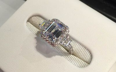 Silver ring with a large rectangular gemstone and small pink accent stones on a white textured display surface