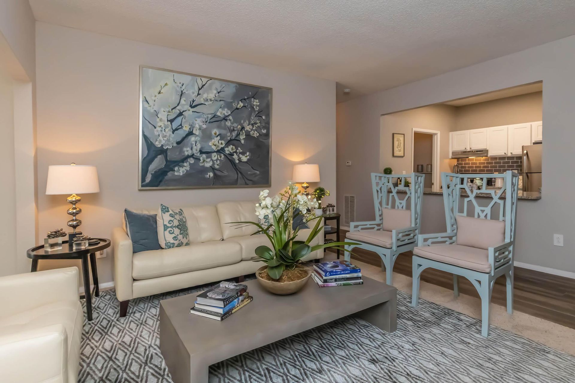 Living room with couch, chairs, coffee table, and open kitchen. Gray and blue color scheme.