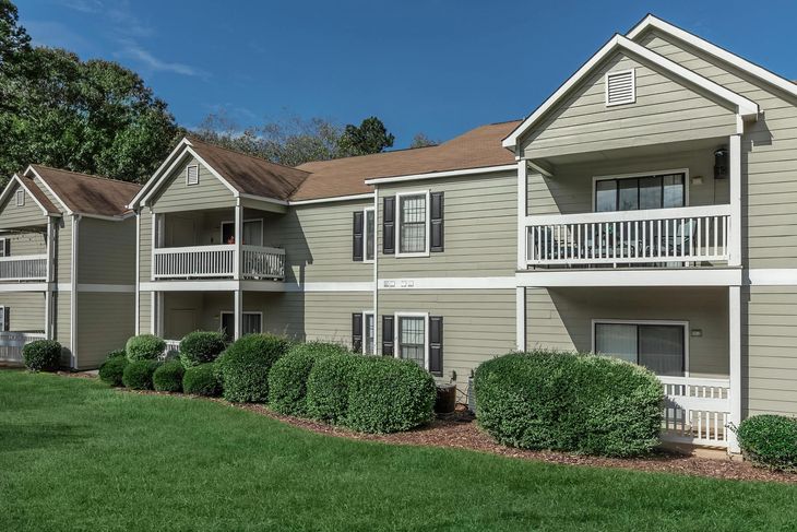 Two-story apartment building with light green siding, brown roof, and small balconies on a grassy lawn.