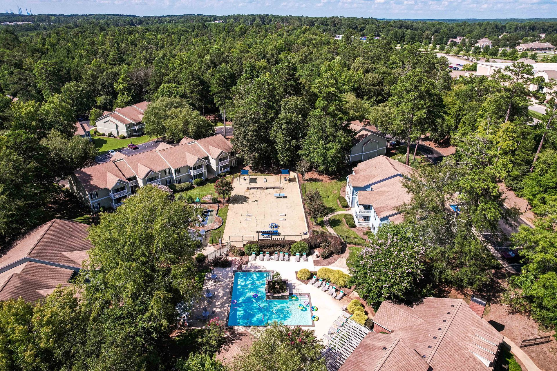 Aerial view of apartments with a pool and volleyball court surrounded by trees.