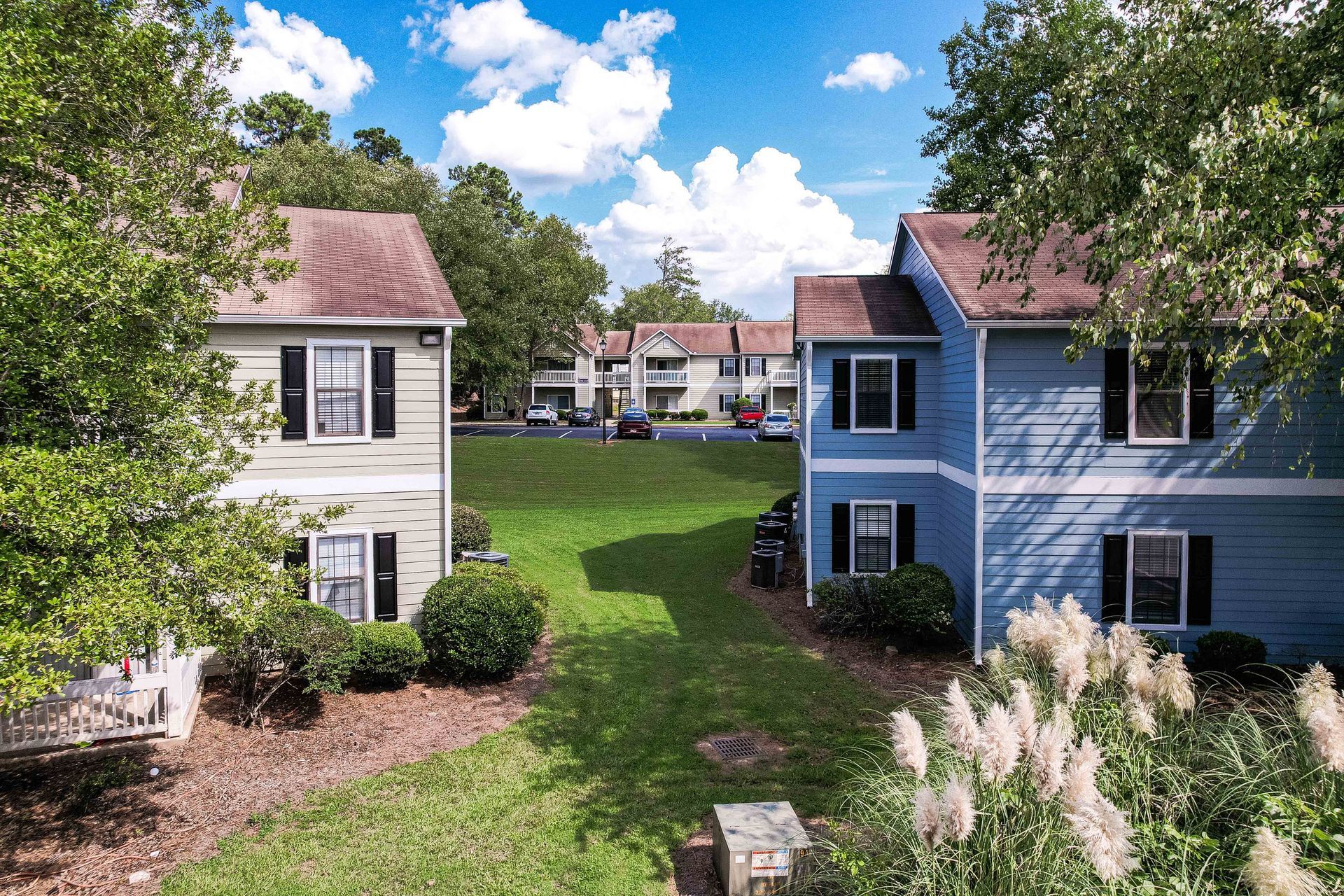 Two-story houses in green and blue, with black shutters, on either side of a green lawn, under a blue sky.