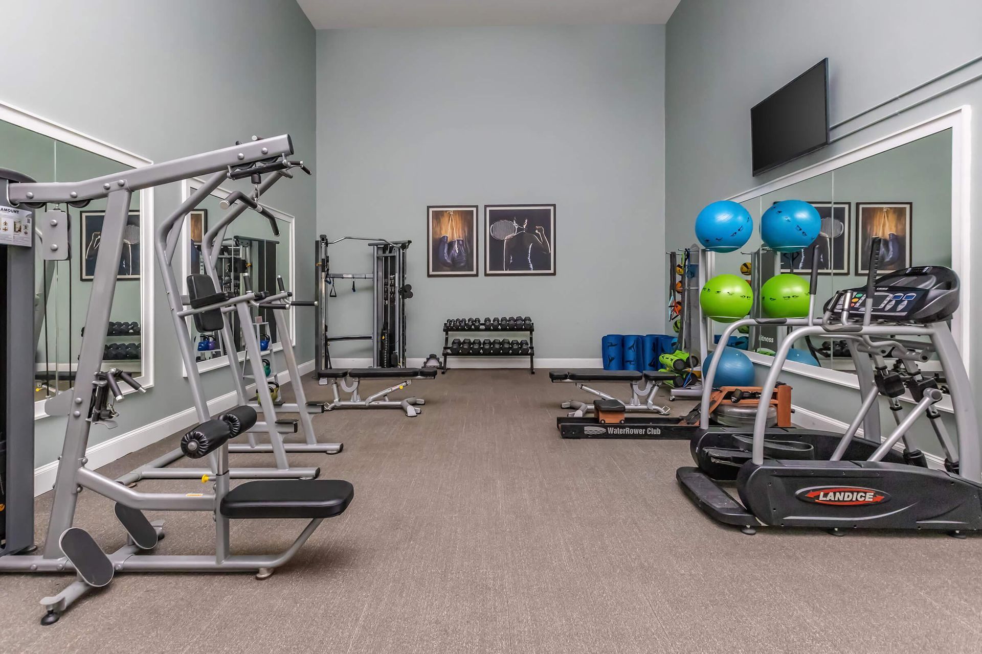 Gym with weight machines, free weights, exercise balls, and a treadmill; gray walls.