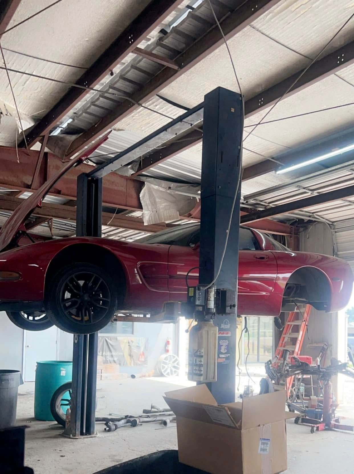 A red sports car is on a lift in a garage.