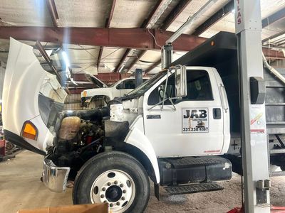 A dump truck is sitting on a lift in a garage with its hood up.