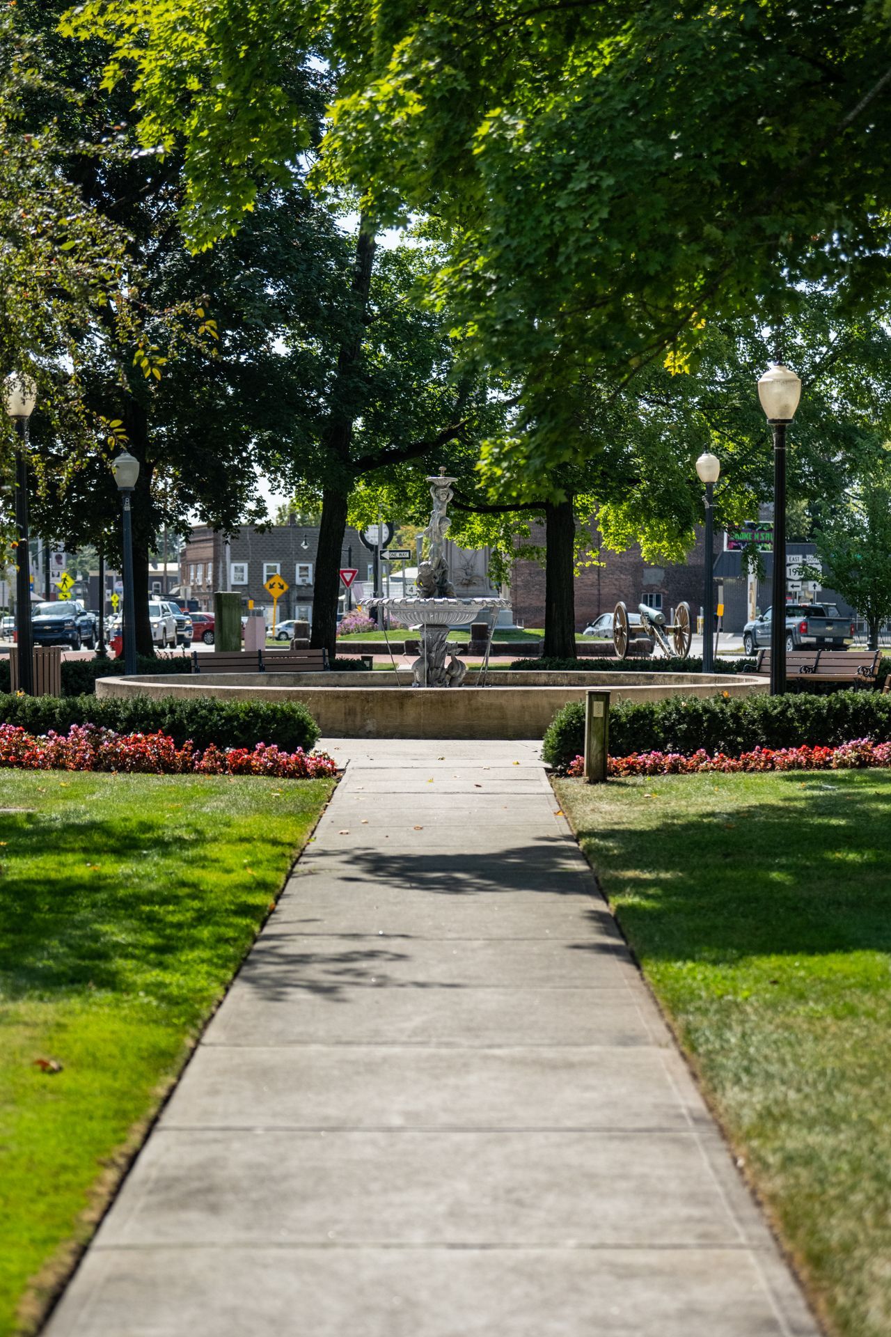 A concrete walkway leading to a fountain in a park