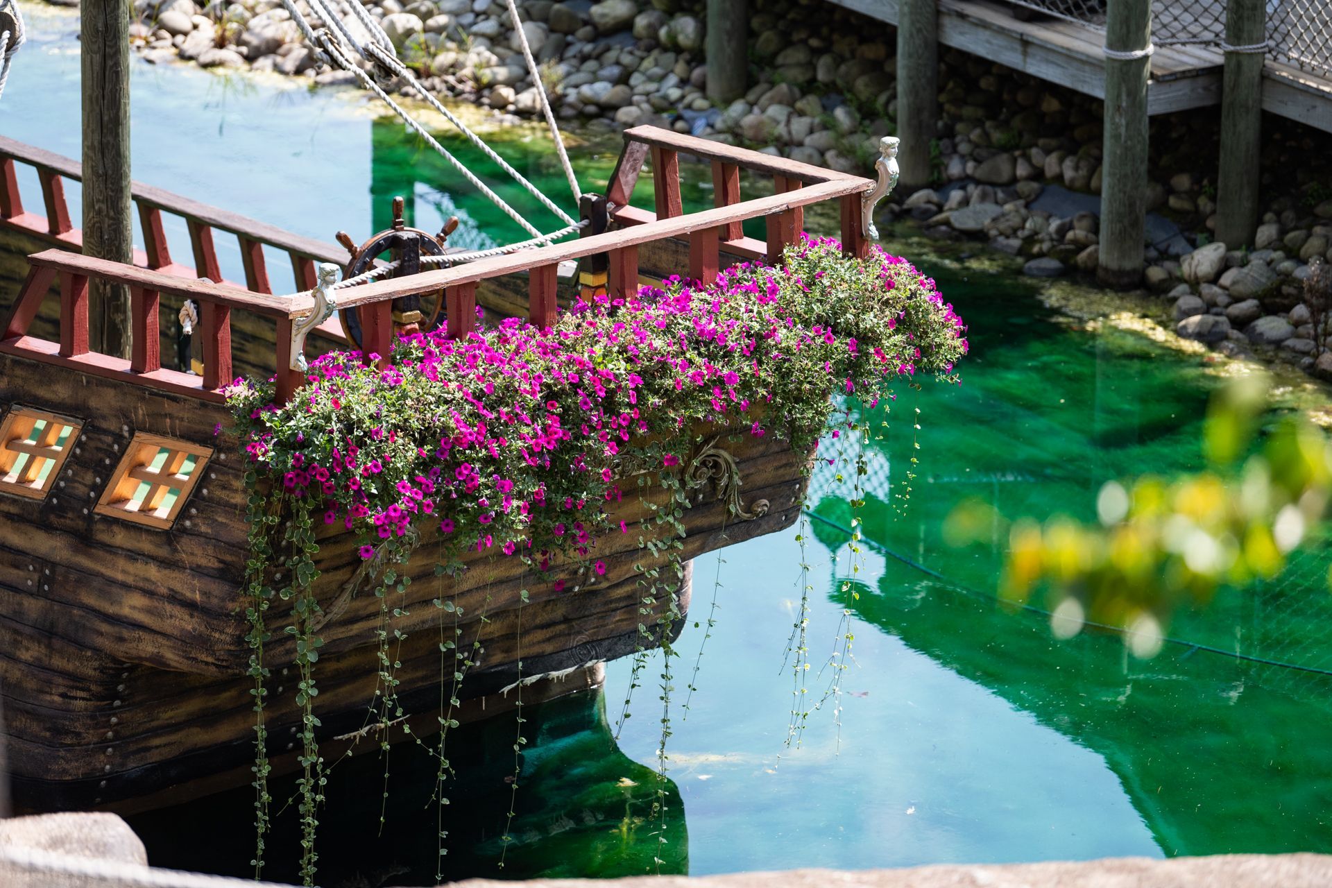 A wooden pirate ship filled with purple flowers is floating on top of a body of water.