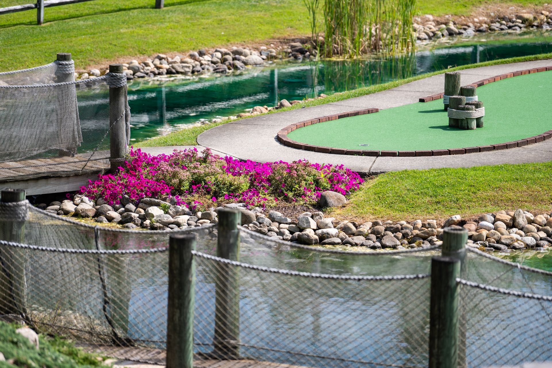 A mini golf course with a fence and a pond in the background.