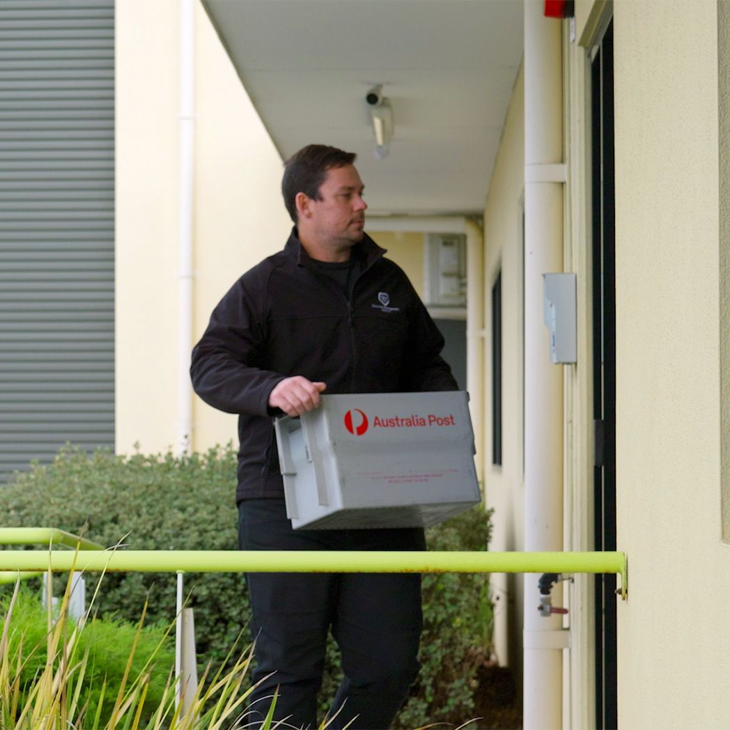Delivery person with Australian Post box approaching a building entrance.