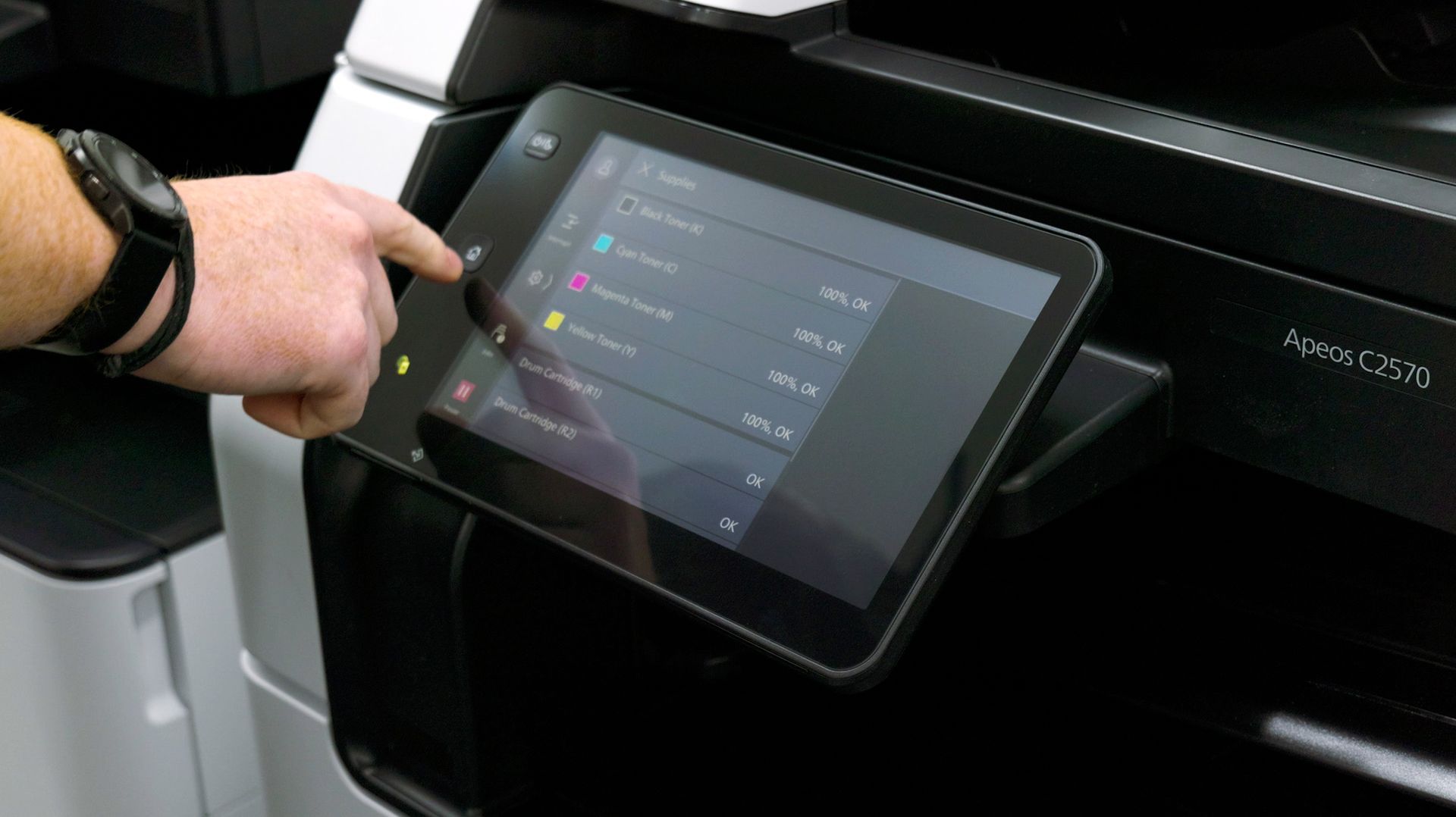 Hand pressing a printer touchscreen; showing options, machine is black.