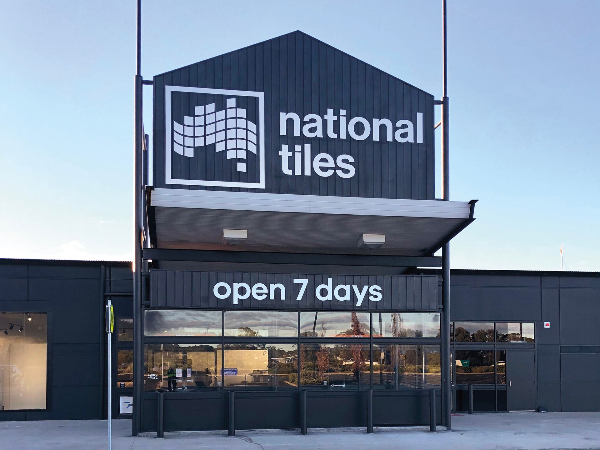 Signage on the exterior for National Tiles store with a dark facade, awning, and