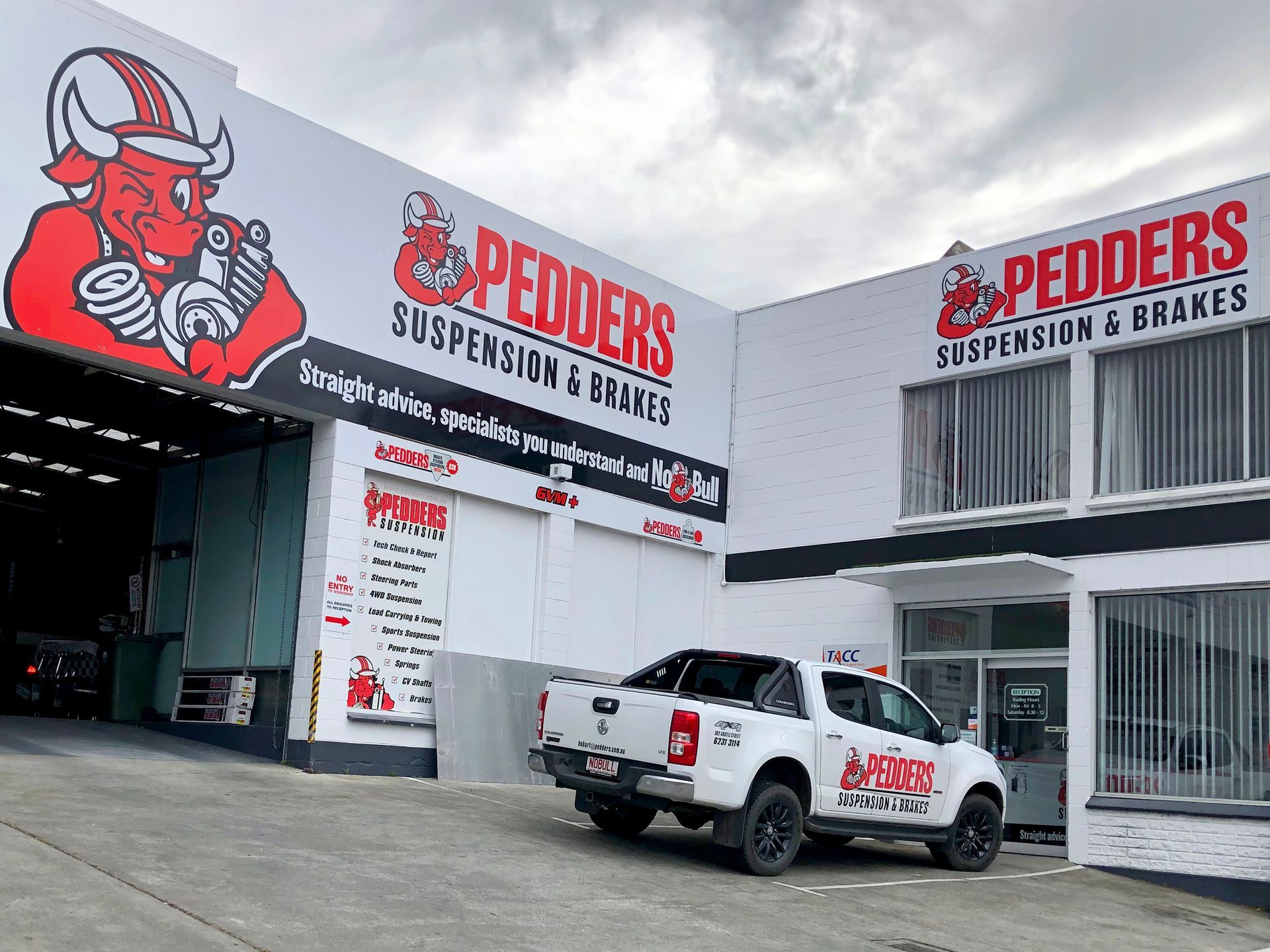 Pedders Suspension & Brakes shop exterior with a truck in front. Red bull logo, white building, cloudy sky.
