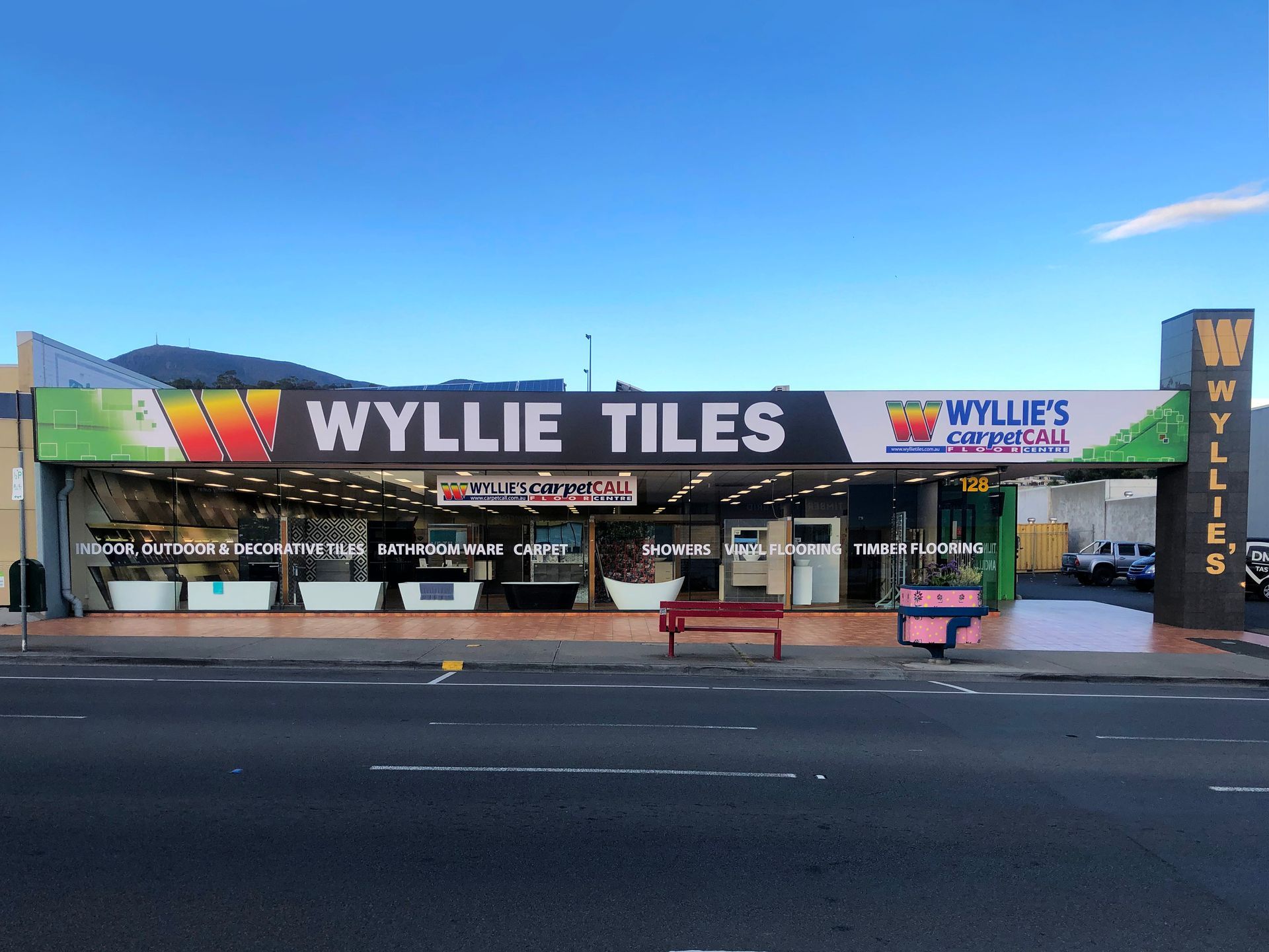 Wyllie Tiles store front. A large commercial building with signage and displays of tiles visible. Bright colors, blue sky.