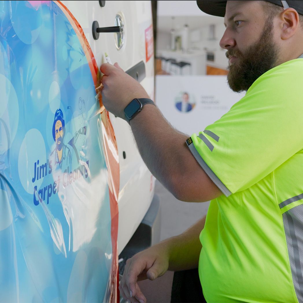 Man in neon shirt applies a decal to a van with 