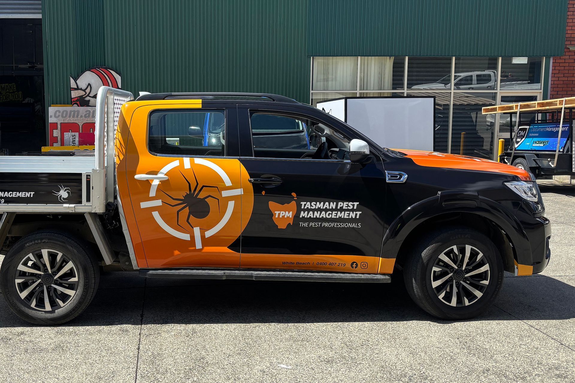 Orange and black pest control truck with spider logo parked outside a building. After carwrap - Tasman Pest Management