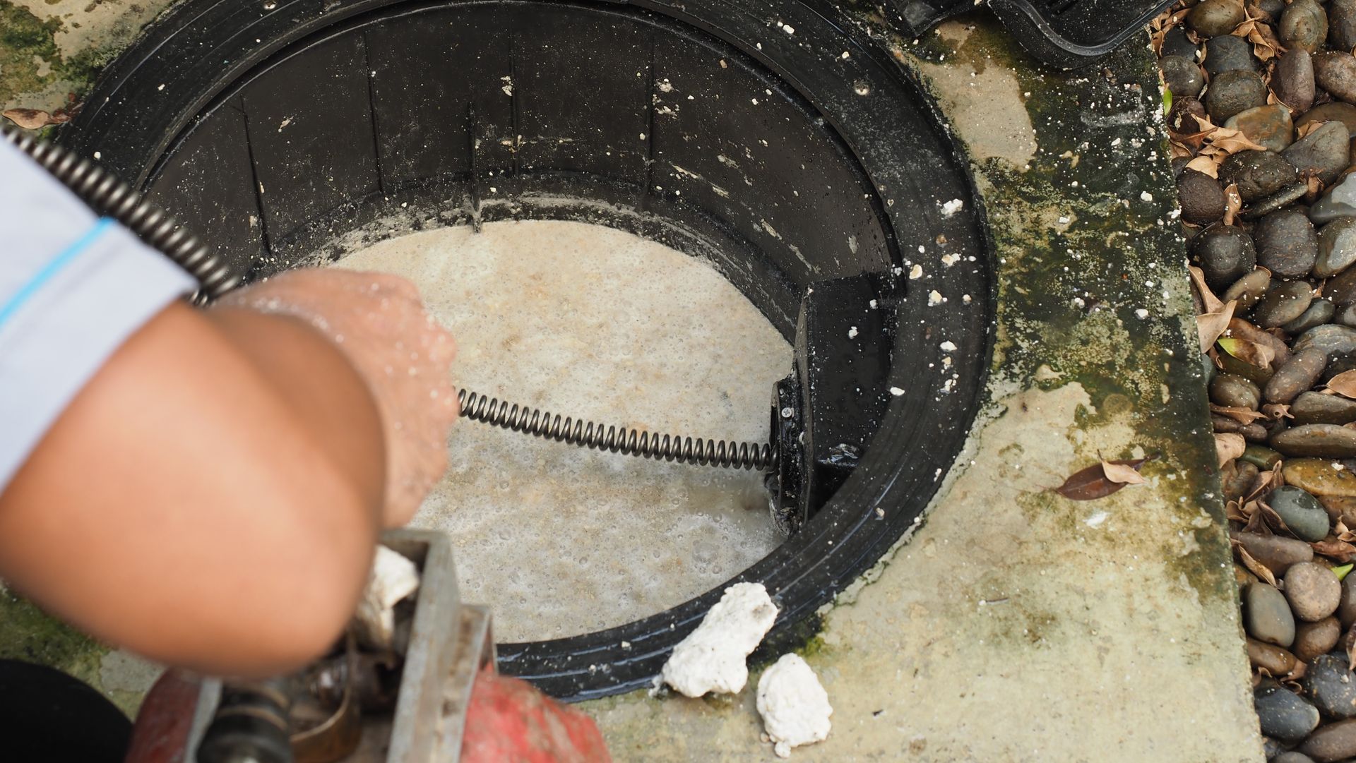 A person is cleaning a manhole cover with a hose.