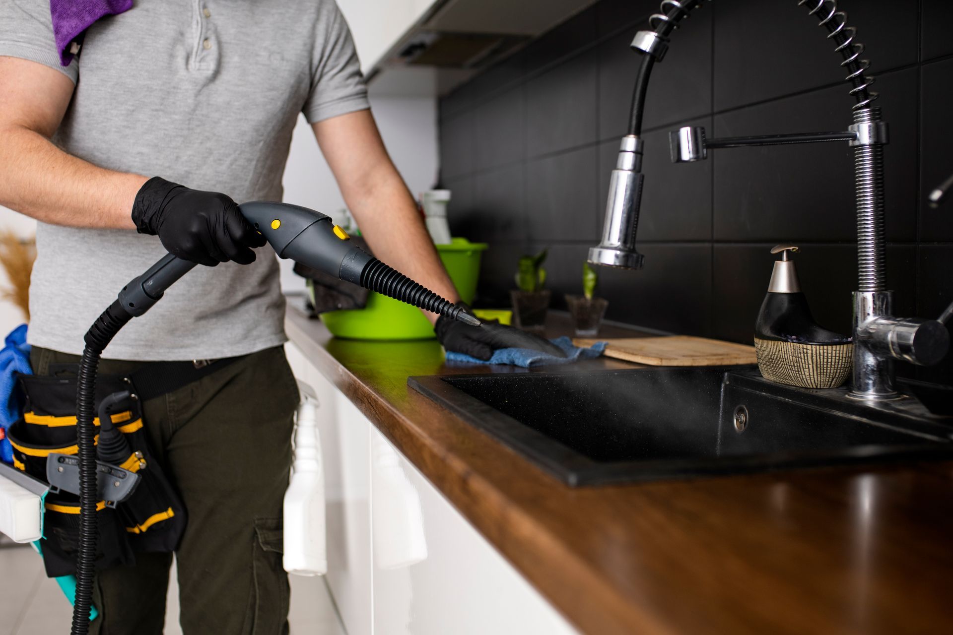 A man is cleaning a kitchen counter with a steam cleaner.