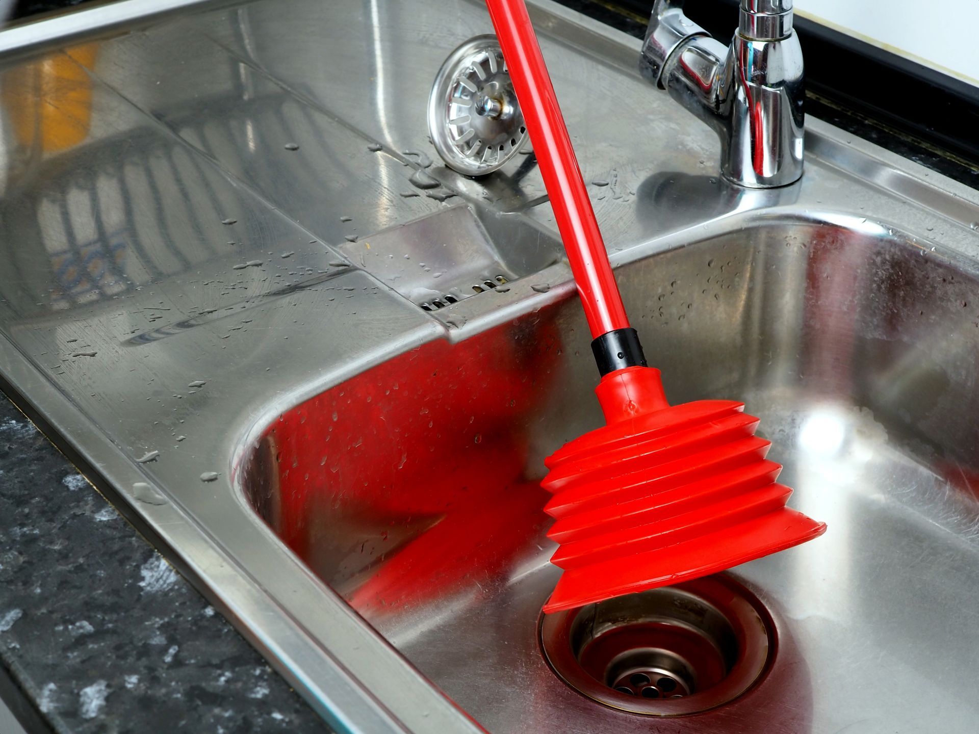 A red plunger is sitting in a kitchen sink.