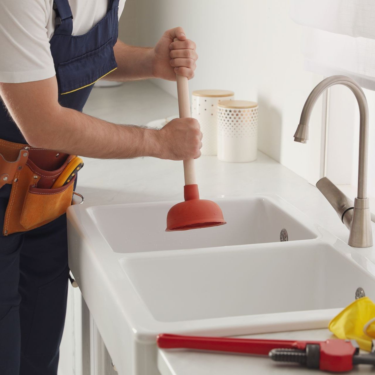 A man is using a plunger to fix a kitchen sink.