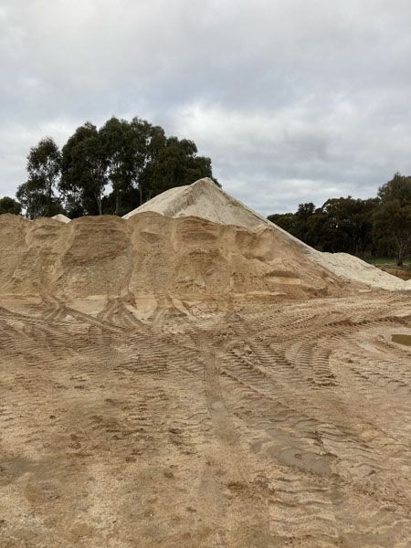 A large pile of sand is sitting on top of a dirt field.