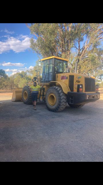 A man is standing next to a yellow bulldozer in a parking lot.