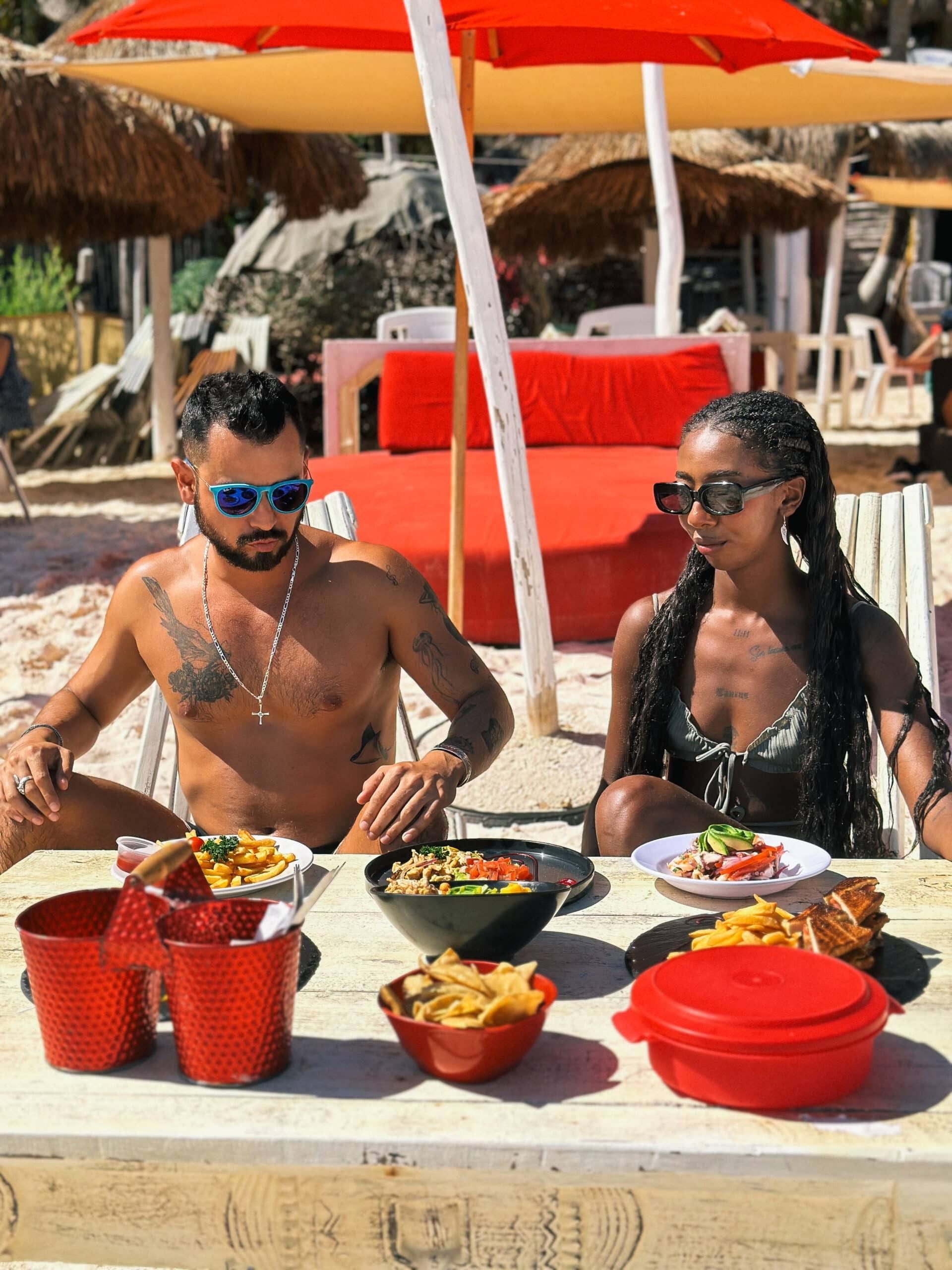 Un hombre y una mujer están sentados en una mesa comiendo comida en la playa.