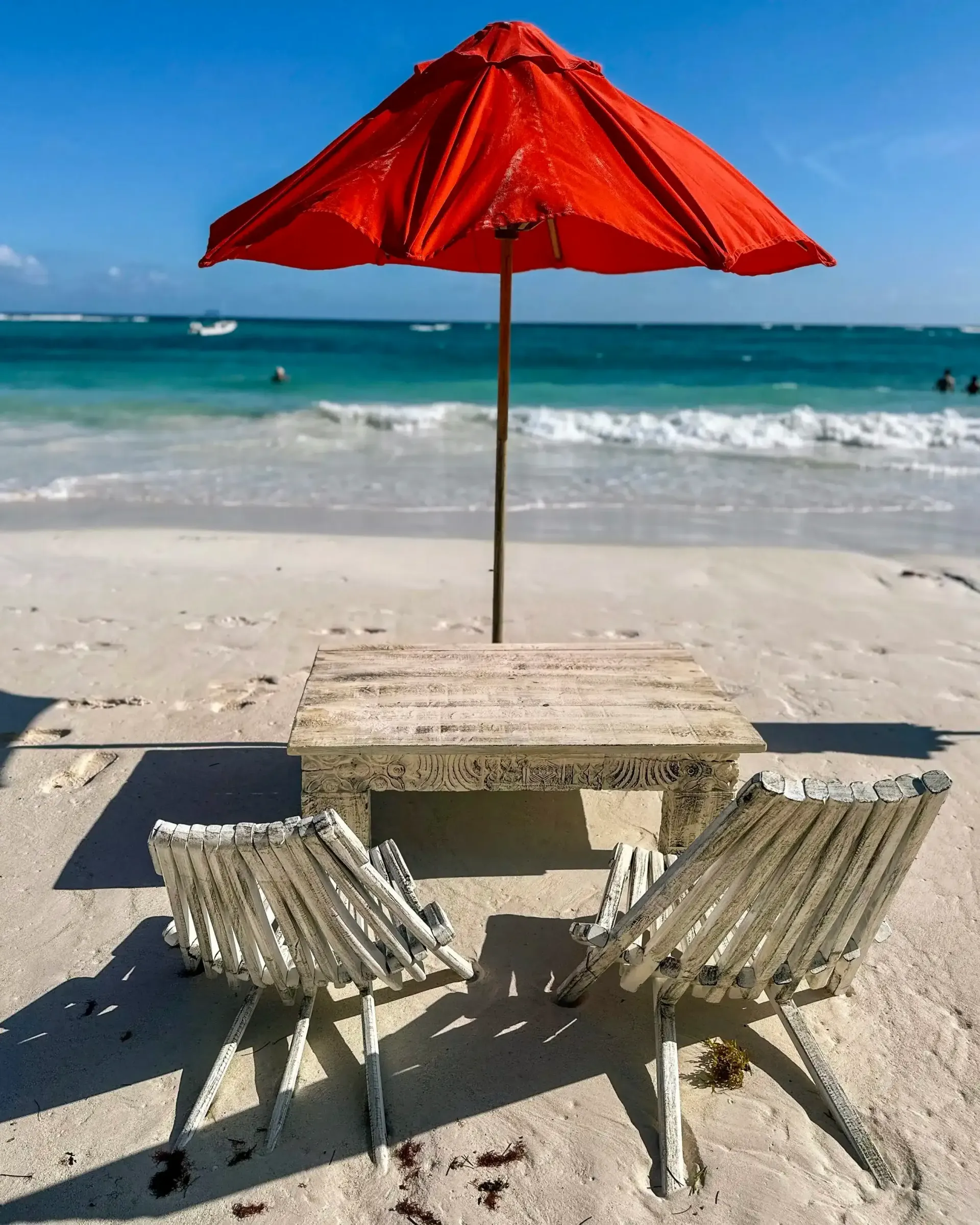 Una sombrilla roja reposa sobre una mesa y sillas en la playa.