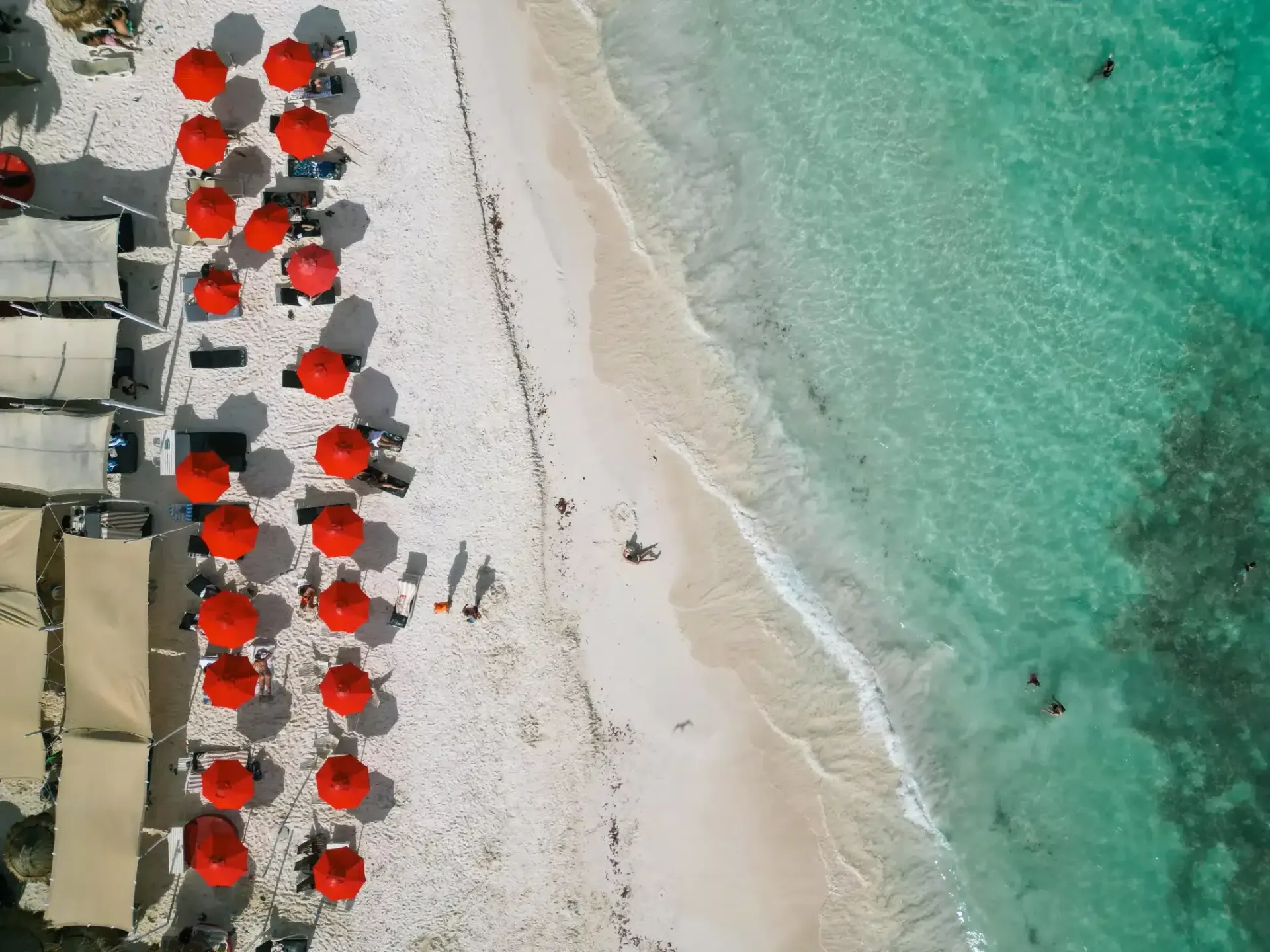 Una vista aérea de una playa con sombrillas y sillas rojas.