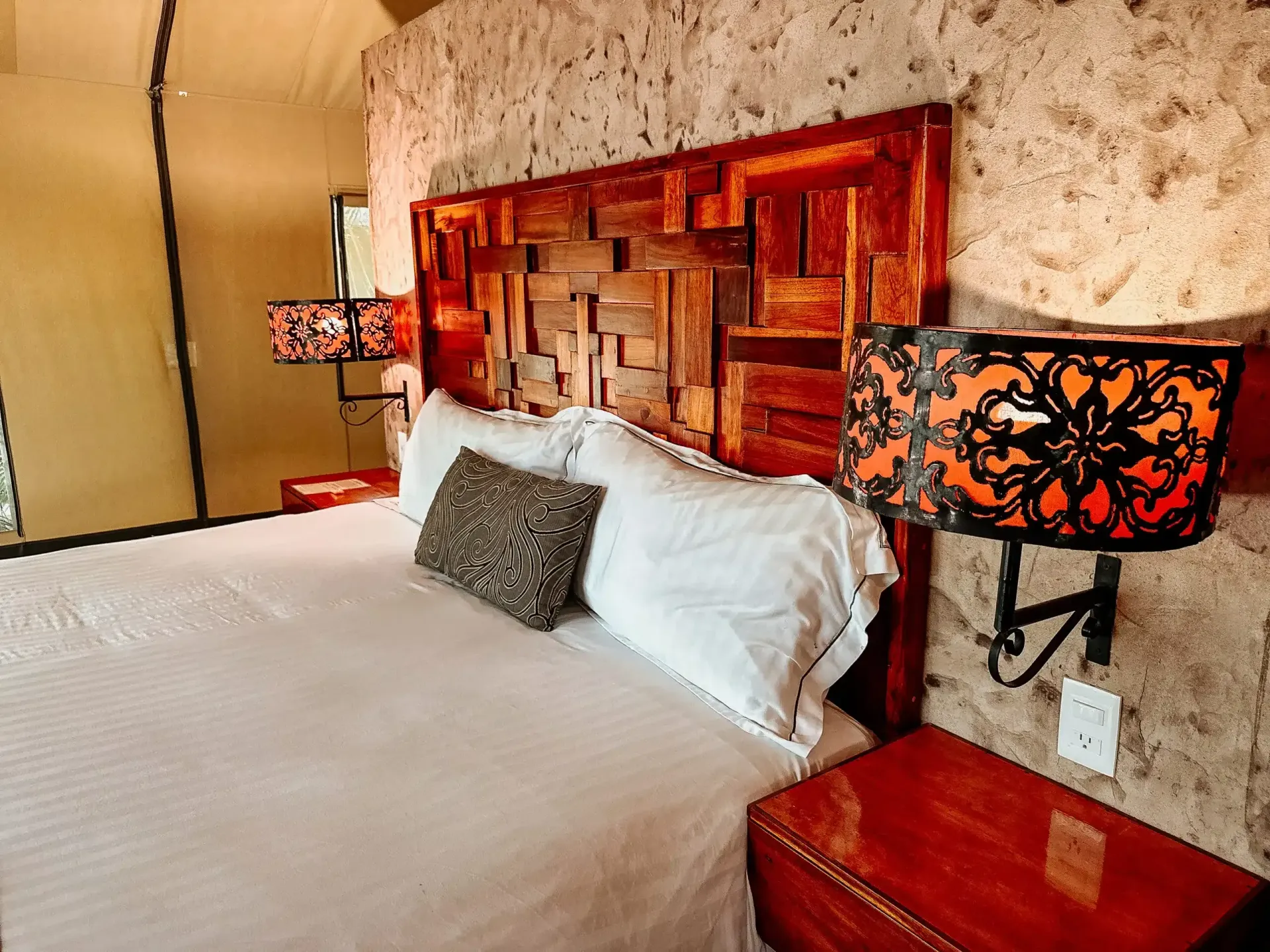 Un dormitorio con una cama, mesita de noche, lámparas y una pared de piedra.