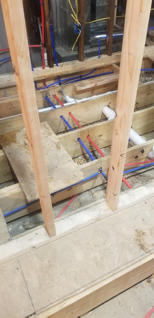 Wooden framing with red and blue water pipes running through it during construction.